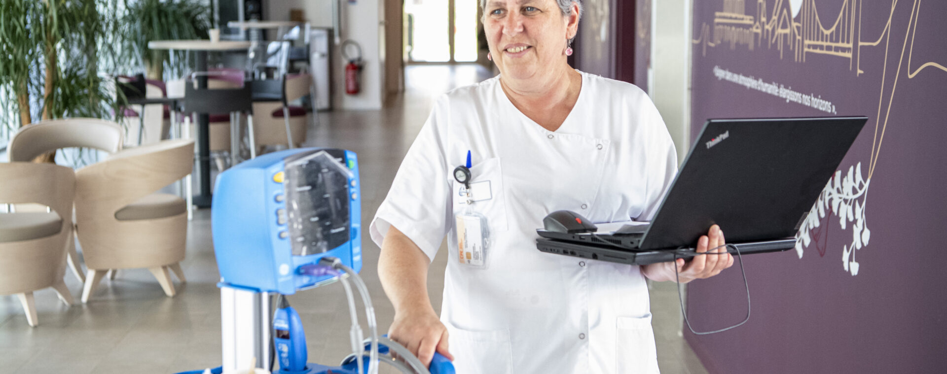 Professionnel de santé circulant dans un service de soins avec un ordinateur portable.